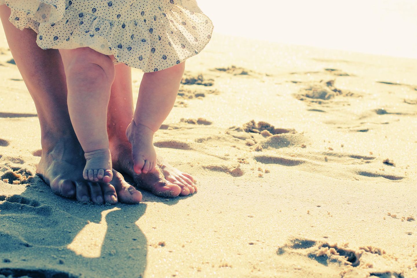 Baby steht auf Füßen der Mutter am Strand