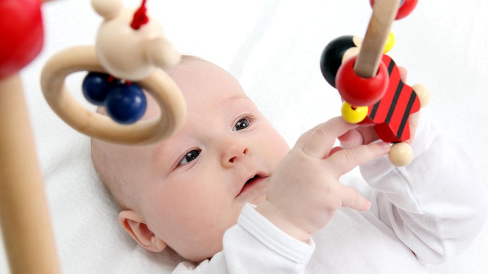 Ein Baby liegt unter einem Spielbogen und spielt mit dem daran befestigten Greifspielzeug.