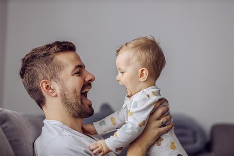 Sprechen lernen: Vater hält seinen kleinen Sohn hoch, beide schauen sich lachend an