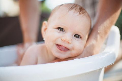 Baby ans Wasser gewöhnen: Baby wird gebadet und schaut in die Kamera