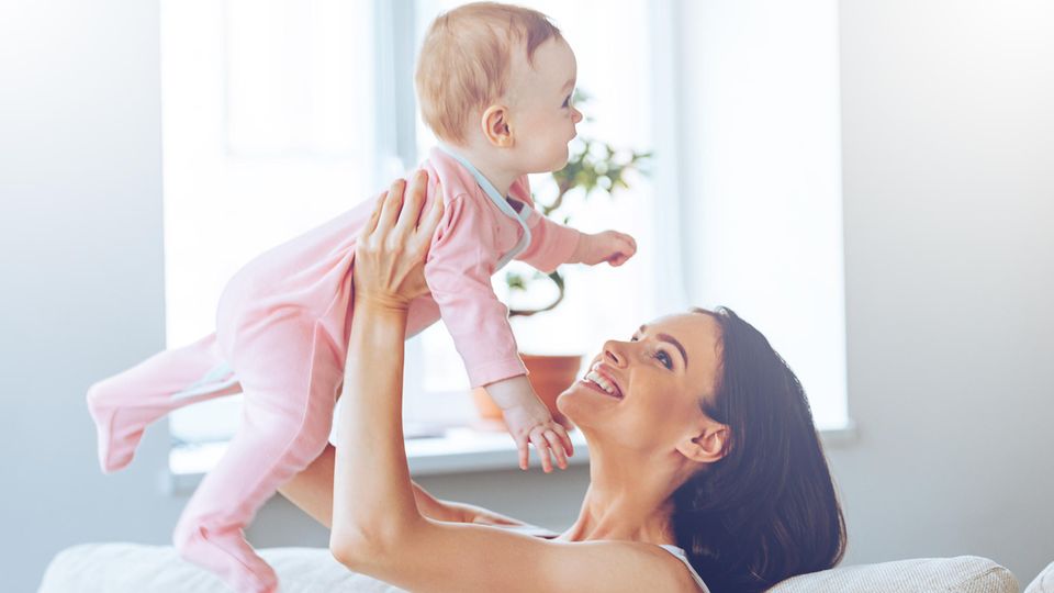 Ein Frau hebt ihr Kind hoch, das sich sehr freut und lacht.