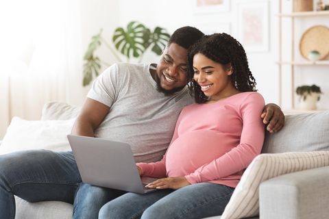 Ein Mann und eine schwangere Frau sitzen auf dem Sofa vor dem Laptop.