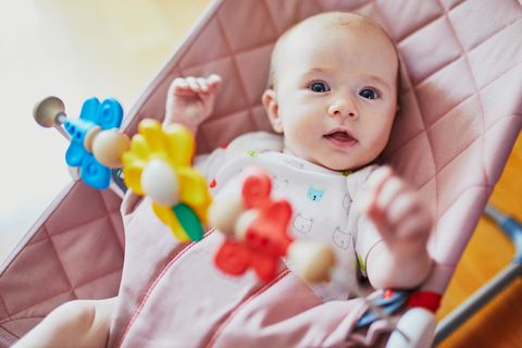 Babywippe im Test: Baby sitzt in rosa Wippe mit bunter Spielzeugkette vor sich.