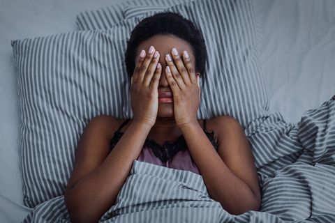 Schlafstörungen bei Müttern: Frau liegt im Bett und hält sich die Augen zu
