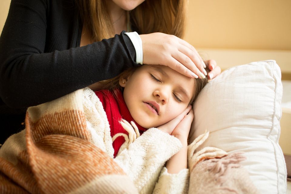 Eine Frau streichelt ihrer kranken Tochter die Stirn.