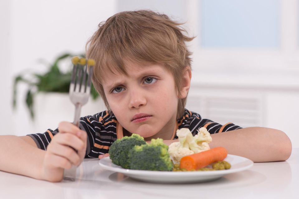 Ein Junge starrt angewidert das Gemüse auf seiner Gabel und seinem Teller an.