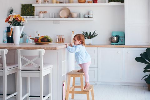 Ein kleines Mädchen klettert auf die Arbeitsfläche einer Küche.