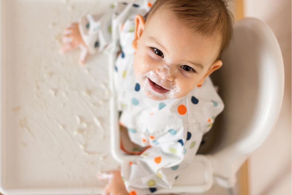 Ein Baby mit verschmiertem Mund lacht nach oben in die Kamera
