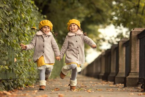 Zwillingsklischees: Lachende Mädchen halten sich an den Händen