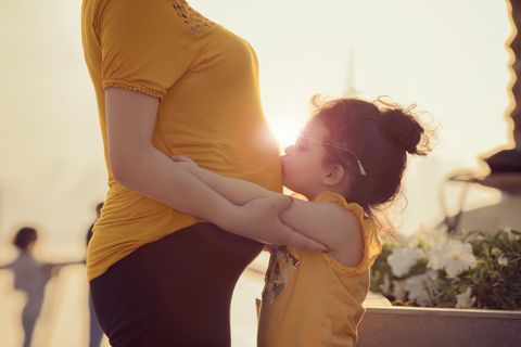 12 Überraschungen, mit denen Eltern beim zweiten Kind nicht rechnen: Kleinkind küsst Bauch der schwangeren Mutter.