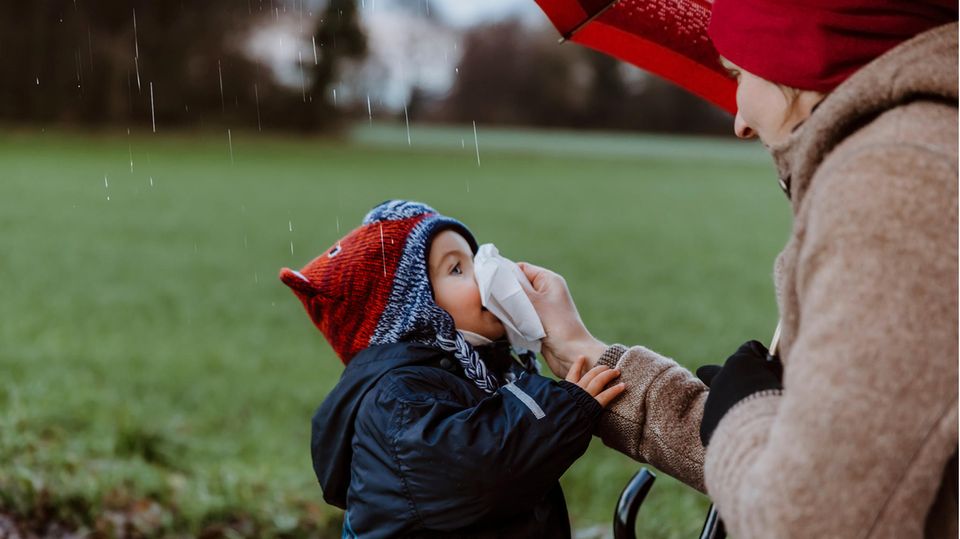 Richtige Kleiderwahl bei Kindern: Mutter putzt Kind die Nase bei Regen