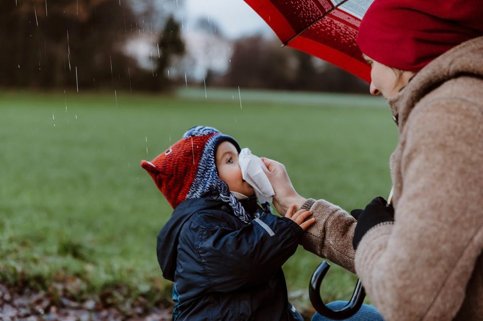 Richtige Kleiderwahl bei Kindern: Mutter putzt Kind die Nase bei Regen