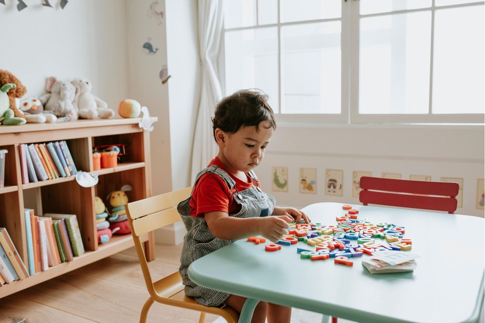 Ein Kleinkind sitzt an einem Tisch und spielt mit Buchstaben