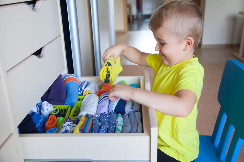 Ein Junge räumt Kleidung in eine Kommode ein