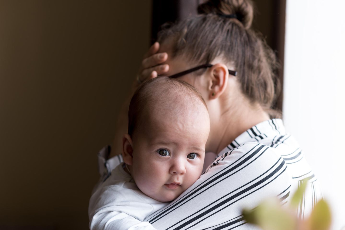 Mama mit Migräne: Mutter mit Baby im Arm hält sich die Hand an die Stirn