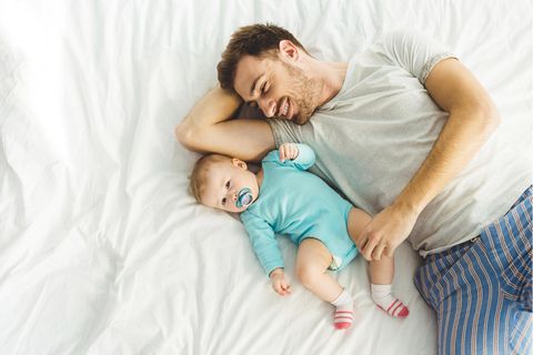 Ein Mann und ein Baby mit Schnuller liegen im Bett.