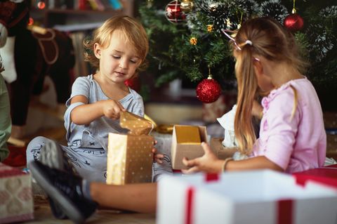 Nachhaltige Weihnachtsgeschenke: Kleines Mädchen am Weihnachtsbaum hält freudig ihr Geschenk in der Hand