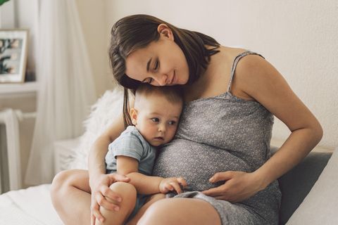 Mutter und erstes Kind kuscheln und streicheln schwangeren Bauch.