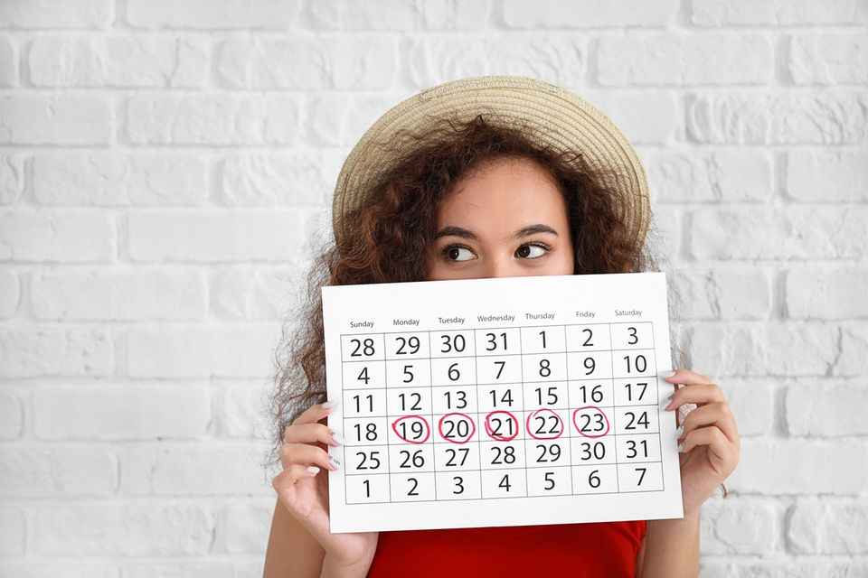 Frau hält Kalender mit markierten Tagen vor ihr Gesicht.