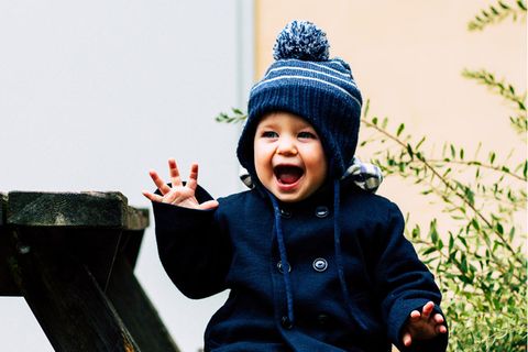 Ein Kleinkind sitzt auf einer Bank und lacht fröhlich.