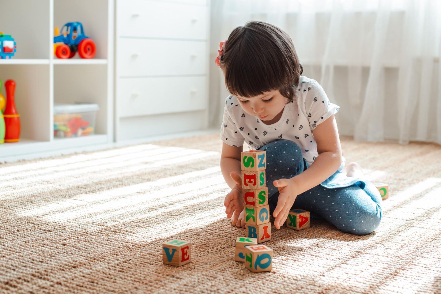 Spielzeug für 3-Jährige: Mädchen im Kinderzimmer hat einem Turm aus Bauklötzen gebaut.