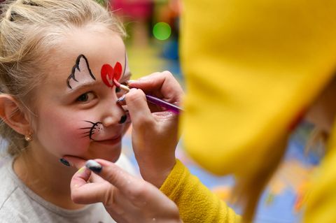 Schmink-Motive für Kinder: Ein blondes Mädchen bekommt ein Herz auf die Stirn gemalt