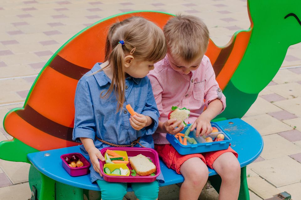 Bento-Boxen für Kinder: Zwei Kinder essen Brote und Gemüsesticks aus ihren mitgebrachten Bento-Boxen.