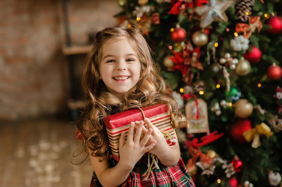 Ein Mädchen mit langen Haaren lächelt und hält ein Weihnachtsgeschenk in ihren Armen