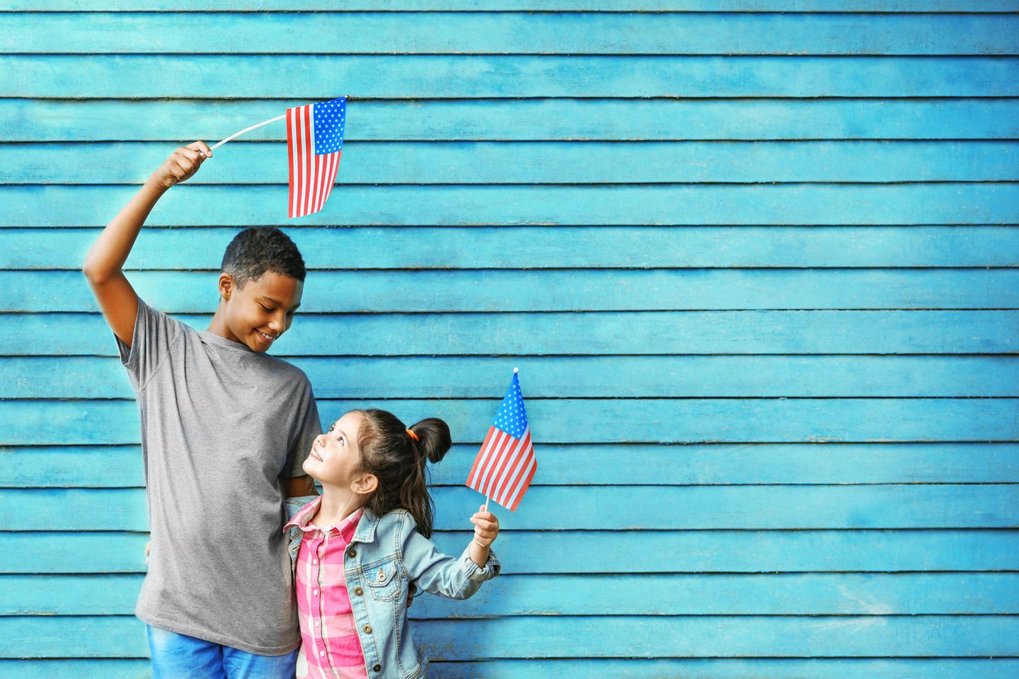 Zwei Kinder stehen vor einem bläulichen Tor und halten amerikanische Fahnen hoch