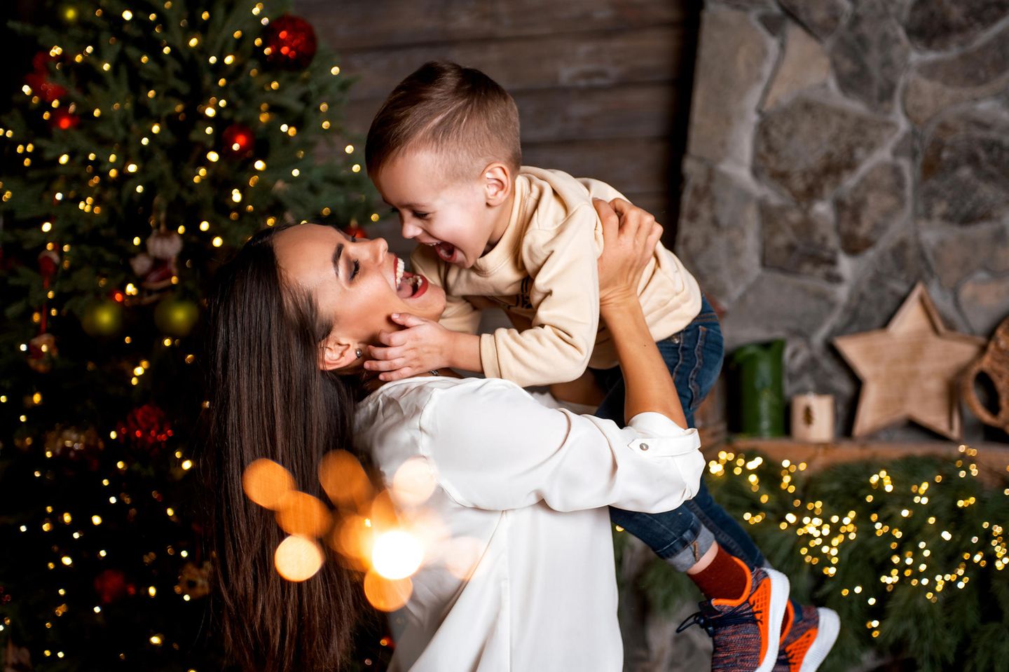 Eine Mutter hält ihren Sohn vor einem Weihnachtsbaum in die Lüfte