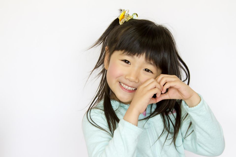 Japanisches Mädchen lächelt und formt ein Herz mit ihren Händen