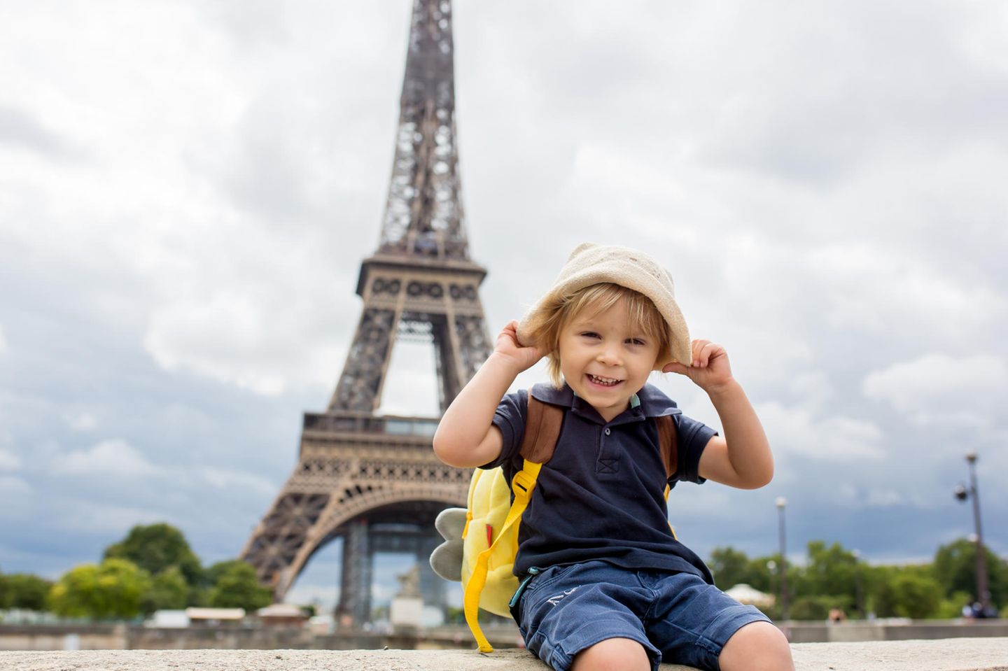 Lachender Junge sitzt auf einer Mauer, der Eiffelturm in Frankreich im Hintergrund