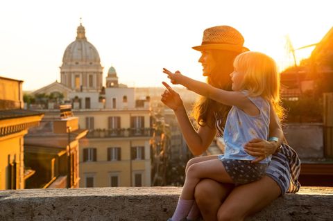 Mutter sitzt auf einer Mauer, Tochter auf dem Schoß, beide blicken auf Rom in Italien