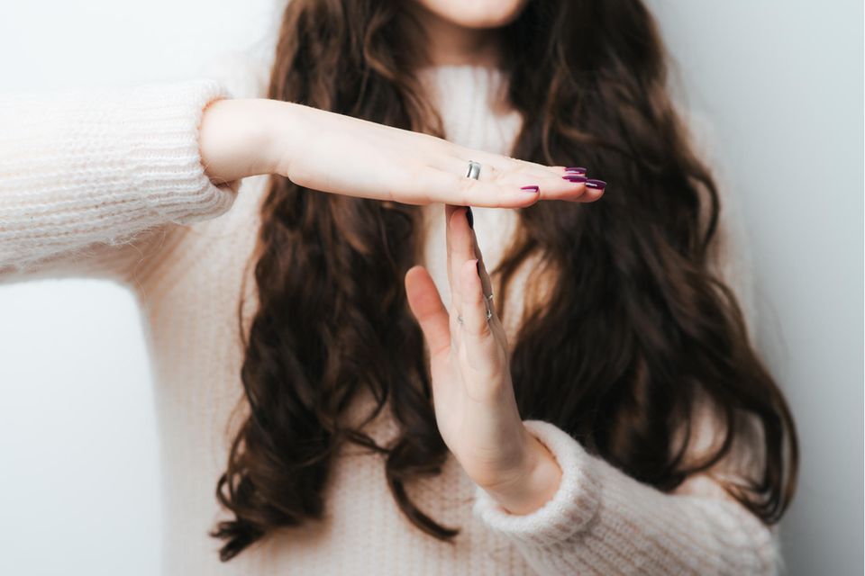 Eine Frau mit langen dunklen Haaren macht mit ihren Händen das Time-Out Zeichen