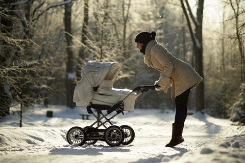 Eine Frau macht einen Spaziergang mit Kinderwagen in winterlicher Landschaft.