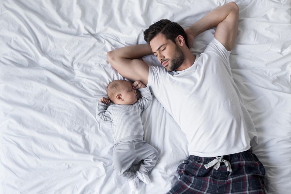 Ein Vater schläft neben seinem Baby