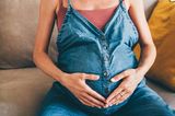 Negative Seiten in der Schwangerschaft: Schwangere mit Latzhose hält sich den Bauch