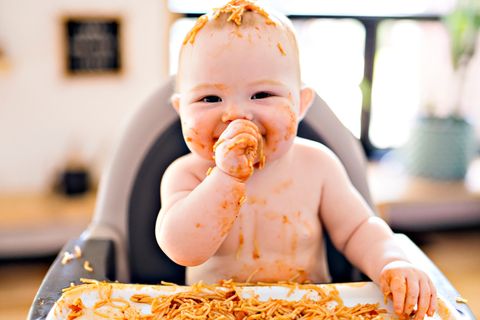 Ein Kleinkind ist mit Nudeln mit Tomatensauce verschmiert und lacht fröhlich.