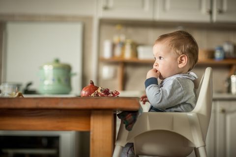 Hochstuhl-Test: Baby sitzt im Hochstuhl am Tischende und isst Granatapfel.