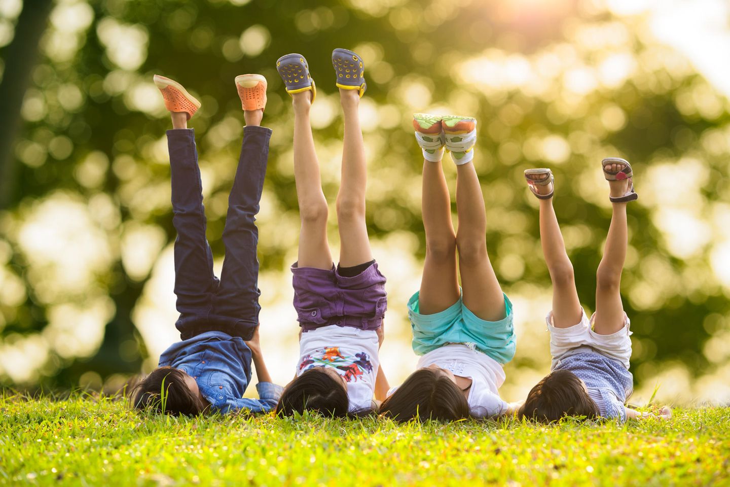 Wahrnehmung: 4 Kinder liegen nebeneinander auf dem Rasen und strecken die Beine in die Luft