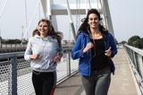 Zwei junge Frauen joggen über eine Brücke