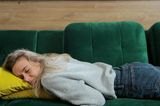 Junge Frau schläft erschöpft auf einem grünen Sofa