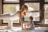 Junge Frau beim Yoga mit ihrem Baby daneben