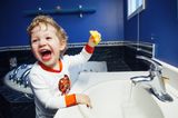 Kleinkind spielt fröhlich mit Wasserhahn im Bad