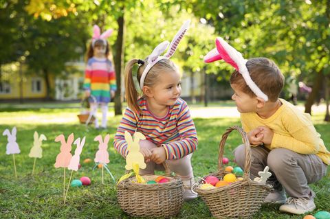 Ostergeschenke für Kinder: Junge und Mädchen mit Hasenohren und vollem Osterkörbchen im Park.