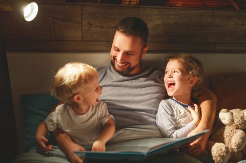 Osterbücher für Kinder: Vater lacht mit zwei Kindern über einem Bilderbuch.