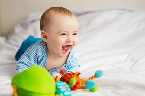 Ein Baby liegt mit Spielzeug im Bett und lacht