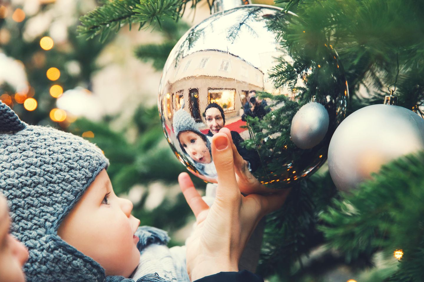 Mein erstes Weihnachten: ein Baby spiegelt sich in einer silbernen Tannenbaumkugel