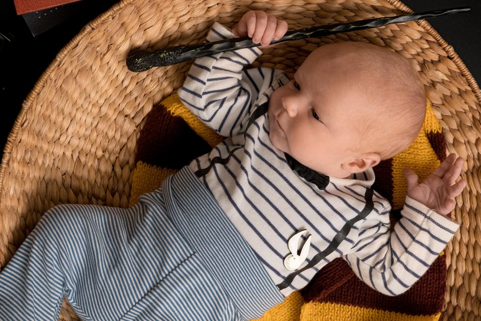Ein Baby liegt mit Zauberstab und Gryffindor Schal in einem Körbchen