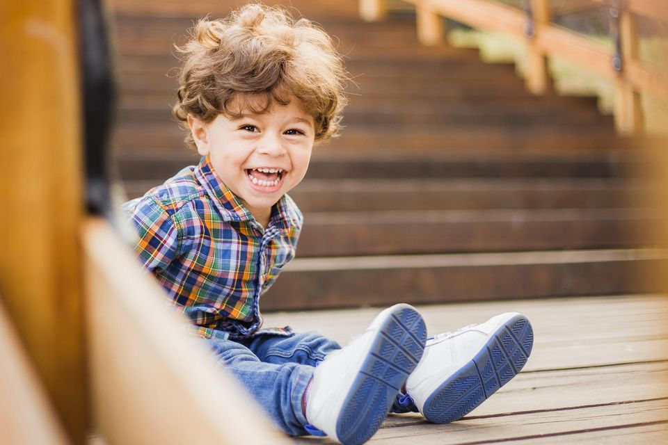Ein kleiner Junge sitzt draußen auf einer Holztreppe und lacht